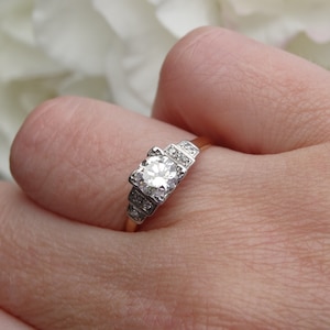 May include: A vintage engagement ring with a central round diamond surrounded by smaller diamonds. The ring is set in a gold band.
