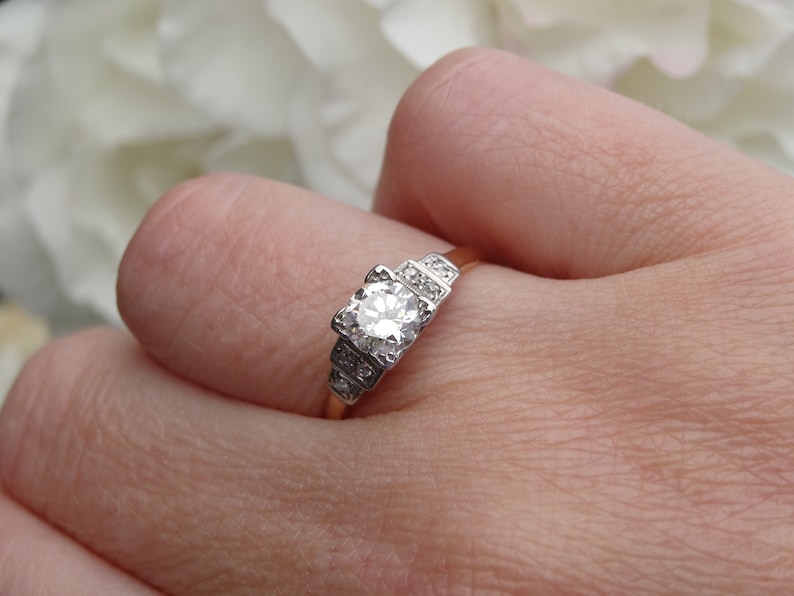 May include: A vintage engagement ring with a central round diamond surrounded by smaller diamonds. The ring is set in a gold band.