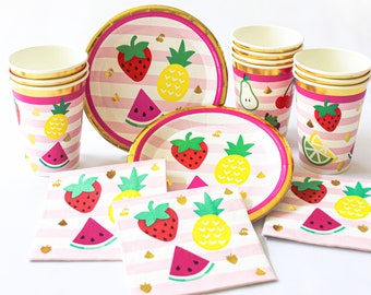 May include: A set of party supplies featuring paper plates, cups, and napkins with a pink and white striped background. The items are decorated with colorful fruit illustrations including strawberries, pineapples, and watermelon slices.