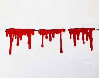 May include: Red glitter paper blood drop garland for Halloween decorations. The garland is strung on a black thread and has multiple red glitter paper blood drops.
