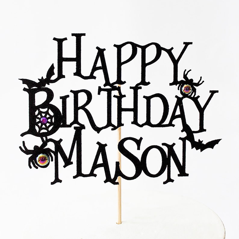 May include: Black cake topper with the text "Happy Birthday Mason" in a spooky font. The topper features bats, spiders, and spiderwebs.