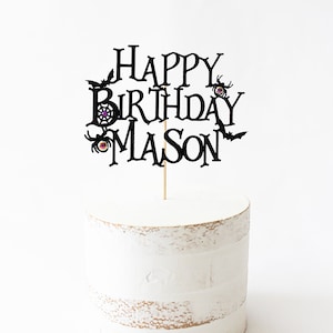 May include: Black cake topper with the text "Happy Birthday Mason" in a spooky font. The topper features bats, spiders, and spiderwebs.