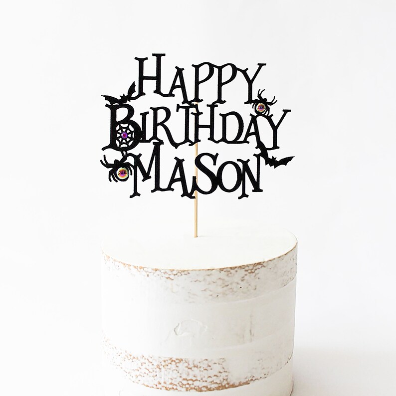 May include: Black cake topper with the text "Happy Birthday Mason" in a spooky font. The topper features bats, spiders, and spiderwebs.