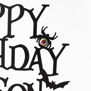 May include: Black and white card with the words "Happy Birthday" in a gothic font. A black spider with a glittery iridescent eye is perched on the "Y" in "Birthday".