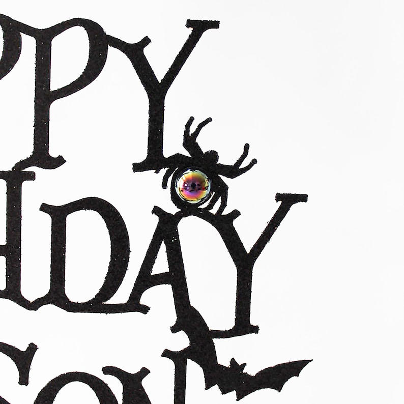 May include: Black and white card with the words "Happy Birthday" in a gothic font. A black spider with a glittery iridescent eye is perched on the "Y" in "Birthday".