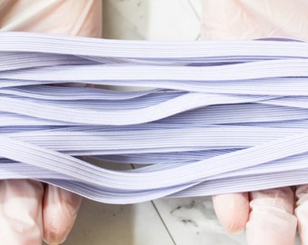 May include: A bundle of light purple elastic bands, tightly packed together. The bands are thin and flat, with a subtle ribbed texture. The image is a close-up, highlighting the color and texture of the elastic. The elastic is held by hands wearing pink gloves.