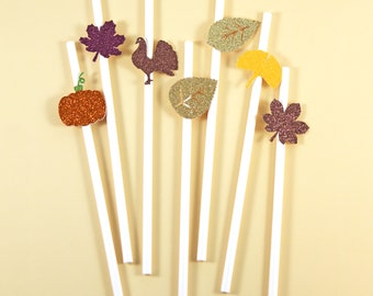 May include: White paper straws with glitter fall-themed decorations, including a pumpkin, leaves, a turkey, and a ginkgo leaf.