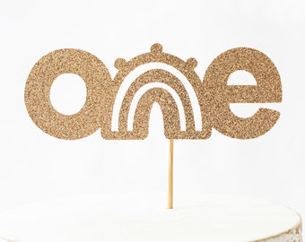 May include: A gold glitter cake topper with the word "one" and a rainbow design. The topper is attached to a wooden stick for easy insertion into a cake. The design is perfect for a first birthday celebration.