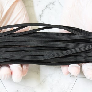 May include: A close-up of a bundle of black elastic cord, held in gloved hands. The cord is tightly wound and appears to be of a good quality.