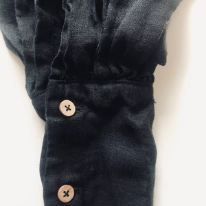 May include: Close-up of a black linen shirt cuff with two wooden buttons. Each button has an 'X' etched into the surface.
