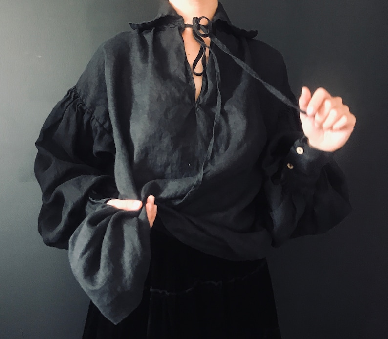 May include: A black linen shirt with a gathered neckline and long sleeves. The shirt has a tie at the neck and is tied in a knot at the front.