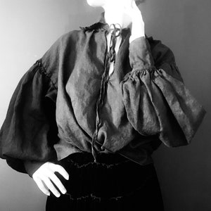 May include: A black blouse with a gathered neckline and long, puffed sleeves. The blouse is made of a soft, flowing fabric and has a relaxed fit.