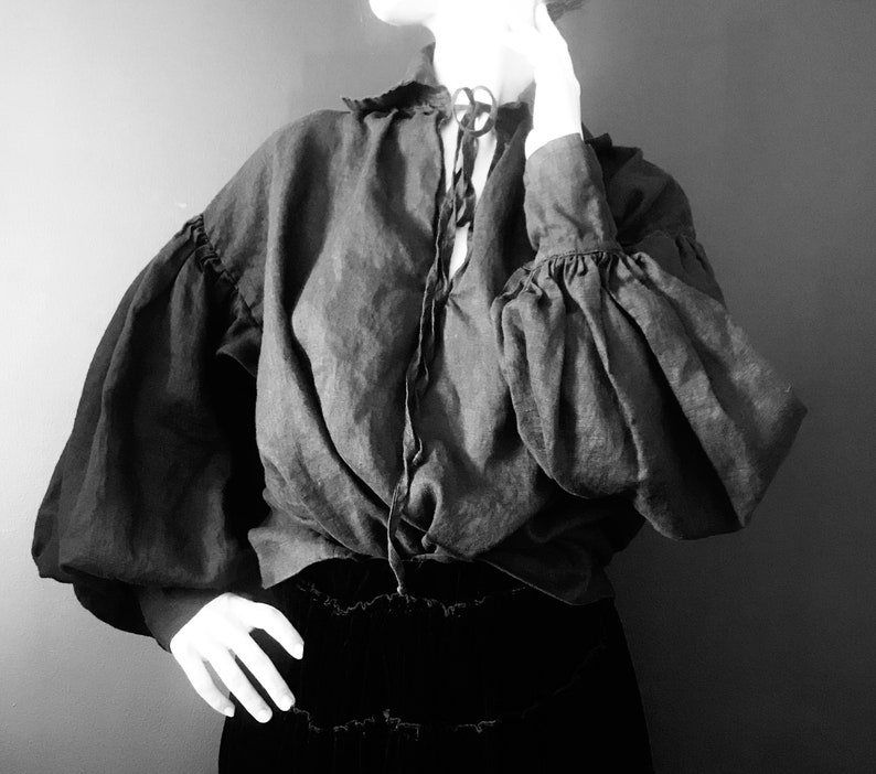 May include: A black blouse with a gathered neckline and long, puffed sleeves. The blouse is made of a soft, flowing fabric and has a relaxed fit.