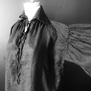 May include: A black linen shirt with a large, gathered collar and long, billowing sleeves. The shirt is tied at the neck with a long, thin cord.