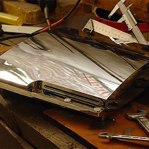 Op de afbeelding: Een zilverkleurige gameconsole met een strak, modern ontwerp. De console staat op een houten oppervlak.