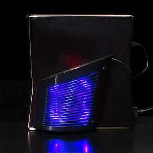 Puede incluir: Un ordenador portátil negro con un ventilador de refrigeración LED azul y morado conectado a la parte posterior.