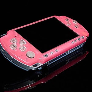 May include: A pink handheld gaming console with a black screen and silver accents. The console has a directional pad, buttons, and a circular button on the front.