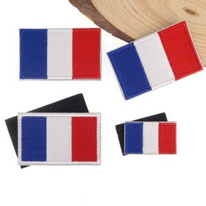 May include: Four rectangular patches featuring the French flag design. Each patch has vertical stripes of blue, white, and red. The patches are on a white surface, with some attached to black fabric.