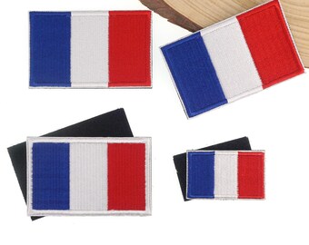 May include: Four rectangular patches featuring the French flag design. Each patch has vertical stripes of blue, white, and red. The patches are on a white surface, with some attached to black fabric.