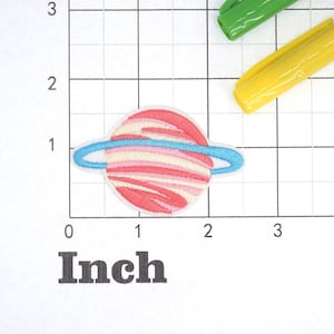 May include: A pink and white striped planet with a blue ring around it. The planet is about 1 inch in diameter.
