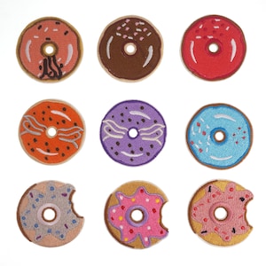 May include: Nine embroidered donut patches in various colors and designs, including pink, blue, purple, orange, and brown. The donuts have sprinkles, icing, and chocolate.