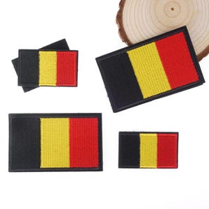 May include: A collection of rectangular patches featuring the flag of Belgium. Each patch has a black vertical stripe, followed by a yellow stripe, and a red stripe. The patches are made of a textured fabric.