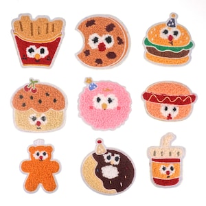 Puede incluir: Nueve parches de fieltro con caras de dibujos animados y diseños de comida. Los parches incluyen una hamburguesa, un cupcake, una dona, una galleta, un hot dog, un vaso de soda, una bolsa de papas fritas, una nube de algodón de azúcar y un oso de peluche.
