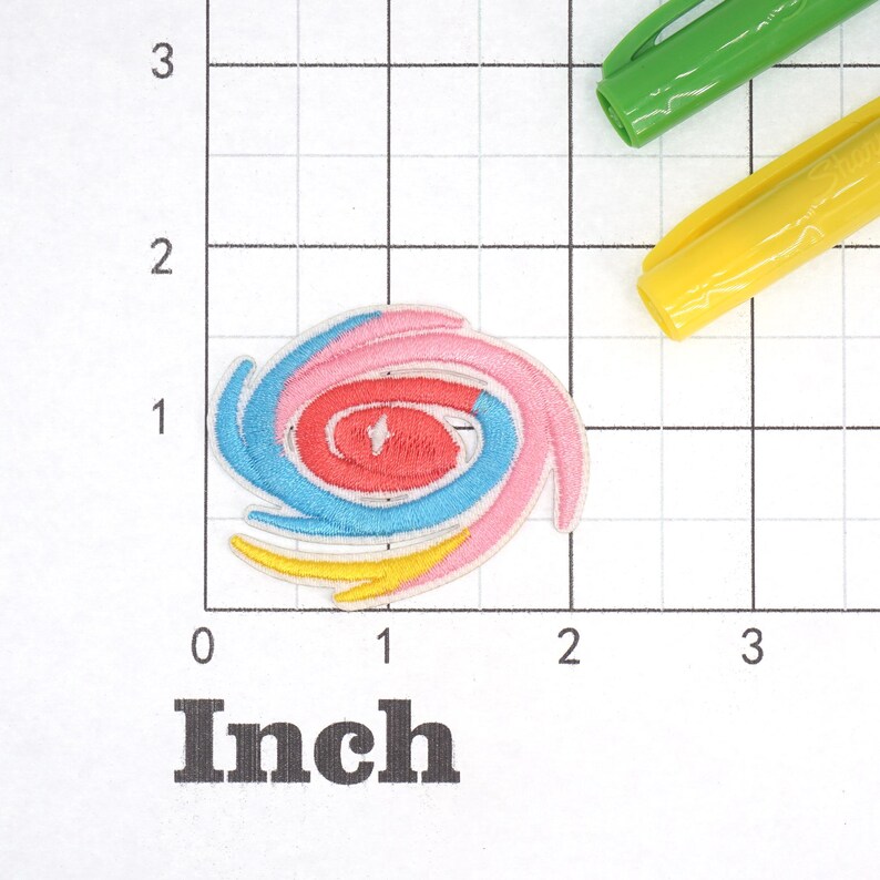 May include: A colorful embroidered patch in the shape of a spiral. The patch is made up of four layers of fabric in pink, red, blue, and yellow.