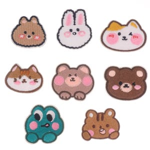 May include: Set of nine embroidered iron-on patches featuring various cute animals, including a bunny, cat, bear, and frog. The patches are all white with brown, pink, and yellow accents.