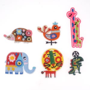 May include: Set of seven colorful embroidered iron-on patches featuring various animals, including a hedgehog, a bird, a giraffe, an elephant, a lion, a dinosaur, and a crocodile.