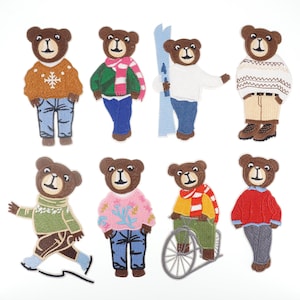 Op de afbeelding: Een verzameling geborduurde berenpatches. Elke beer draagt verschillende outfits, waaronder truien, sjaals en jeans. Eén beer houdt ski's vast, een ander fietst en anderen dragen winterkleding.