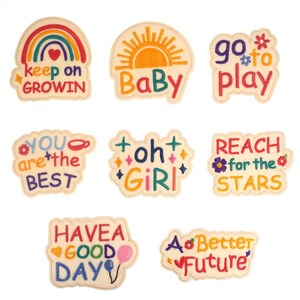 May include: A collection of embroidered patches with positive messages. Designs include a rainbow with "keep on GROWIN", a sun with "BaBy", and "go to play". Other patches say "YOU are the BEST", "oh GIRL", and "REACH for the STARS".