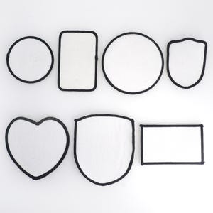 May include: Eight blank iron-on patches in various shapes, including a circle, square, rectangle, heart, and shield. The patches are white with black outlines.