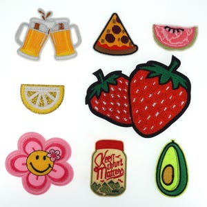 May include: A set of 10 iron-on patches featuring various food and drink designs. The patches include a slice of watermelon, a pizza slice, two glasses of beer, a lemon wedge, two strawberries, a jar with the text "Keep Calm and Matcha On", a smiling flower, and an avocado.