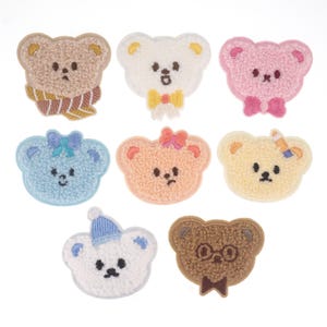 Könnte beinhalten: Satz von neun gestickten Bügelbildern mit niedlichen Teddybären in verschiedenen Farben und Designs. Die Bären haben unterschiedliche Gesichtsausdrücke und Accessoires, darunter Schleifen, Schals und Brillen.