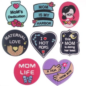 Peut inclure: Dix patchs brodés thermocollants avec différents motifs et couleurs. Les patchs présentent des phrases comme "La Dédicace de Maman", "Maman est mon Havre", "Amour Maternel", "Je Aime les Mamans", "Cette Maman fait de son mieux", "La Vie de Maman" et "Un Bisou de Maman".