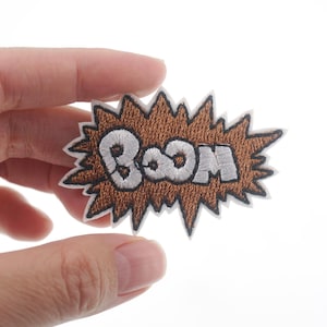 May include: Brown embroidered patch with a white "BOOM" in a comic book style explosion shape.