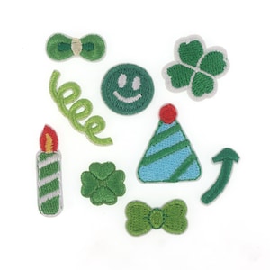 May include: A set of ten green embroidered iron-on patches. The patches include a smiling face, a bow tie, a birthday hat, a candle, a four-leaf clover, a curly ribbon, and an arrow.