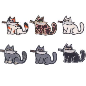 May include: Six embroidered iron-on patches featuring cats with knives. The cats are in various colours and poses, including black, white, grey, and calico.