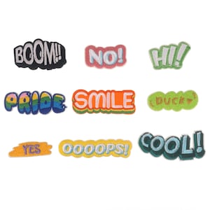May include: Ten colourful iron-on patches with various words and phrases, including "BOOM!" "NO!" "HI!" "PRIDE" "SMILE" "DUCK" "YES" "OOOOPS!" "COOL!"