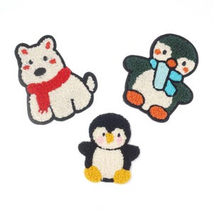 Könnte beinhalten: Drei Filztier-Patches: ein weißer Eisbär mit rotem Schal, ein grüner Pinguin mit blauem Schal und ein schwarz-weißer Pinguin.