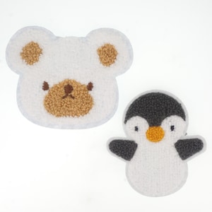 Op de afbeelding: Twee vilt dierlijke applicaties, een witte beer met bruine oren en neus en een witte pinguïn met zwarte vleugels en een gele snavel.