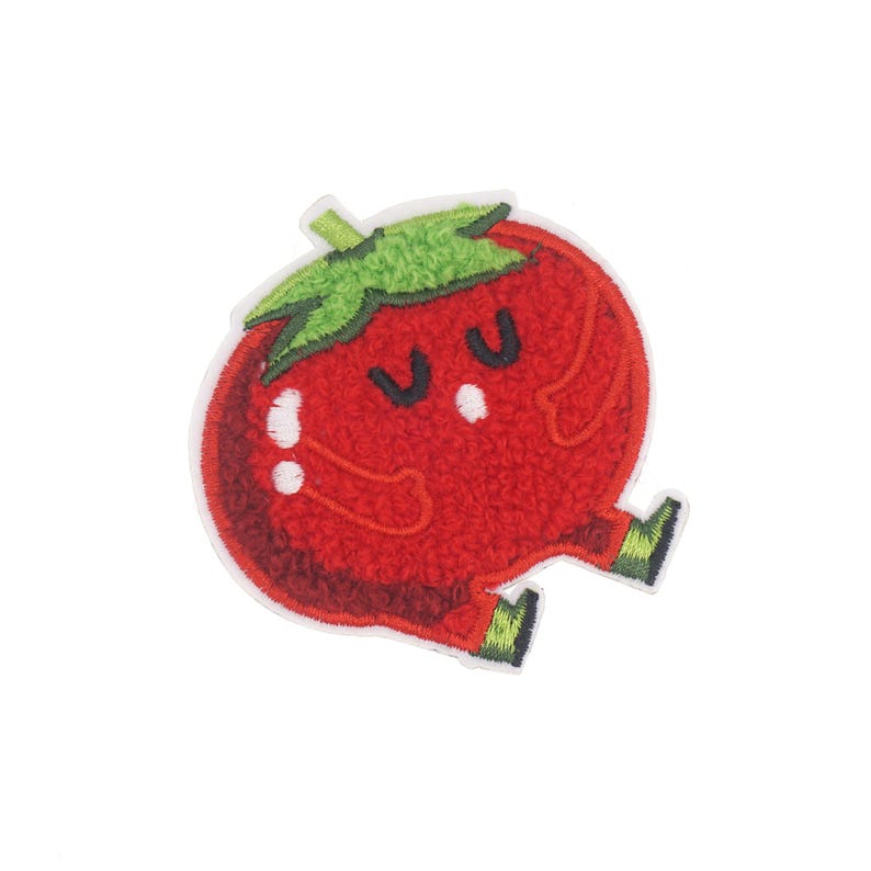 Puede incluir: Parche rojo bordado para planchar de un tomate de dibujos animados con un tallo y hojas verdes. El tomate tiene una cara sonriente con dos puntos blancos para los ojos y una peque&ntilde;a boca.