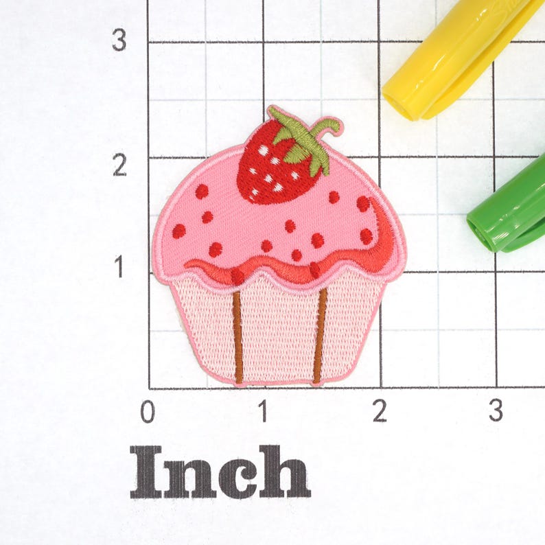 Może przedstawiać: R&oacute;żowy cupcake z czerwoną truskawką na wierzchu. Cupcake ma biały lukier z r&oacute;żowymi posypkami. Cupcake ma około 5 cm szerokości.