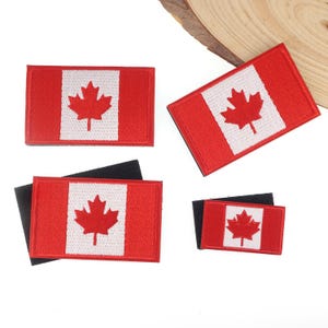 Puede incluir: Cuatro parches rectangulares con la bandera canadiense. Cada parche tiene un campo rojo con un panel central blanco que lleva una hoja de arce roja. Los parches son de diferentes tamaños y tienen un respaldo negro.