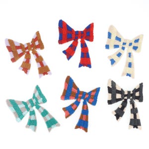 Pode incluir: Seis apliques de laço texturizados e coloridos em vários padrões. Os laços apresentam uma mistura de cores, incluindo vermelho, azul, castanho, verde e preto, com desenhos xadrez e listrados. Estes laços decorativos são adequados para artesanato e embelezamento.