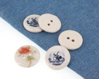 May include: A collection of ceramic buttons in various designs. Some buttons are plain, while others feature hand-painted illustrations of a windmill and a red poppy flower. The buttons are off-white with two holes for sewing.