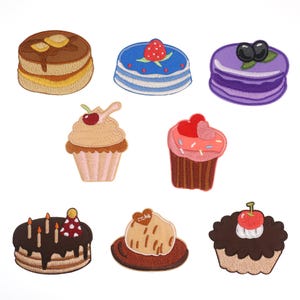 Puede incluir: Surtido de parches bordados para planchar con diferentes dulces, incluyendo un cupcake con una cereza en la parte superior, un pastel con velas, un pastel de chocolate con una cereza en la parte superior, una dona con chispas, un macarrón con arándanos, una pila de panqueques con jarabe, un cupcake con un corazón en la parte superior y un pastel con una fresa en la parte superior.
