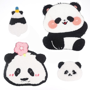 May include: Four plush panda bear patches with black and white fur. One panda has a pink flower on its head, another has a blue and white unicorn horn, and the other two have pink cheeks.