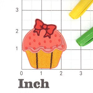 Może przedstawiać: R&oacute;żowo-ż&oacute;łty cupcake z czerwoną kokardką na g&oacute;rze. Cupcake jest ozdobiony białymi kropkami. Cupcake ma około 5 cm szerokości.